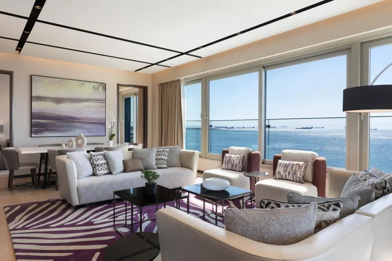 Un salon spacieux avec canapés et fauteuils face à une grande baie vitrée donnant sur la mer.