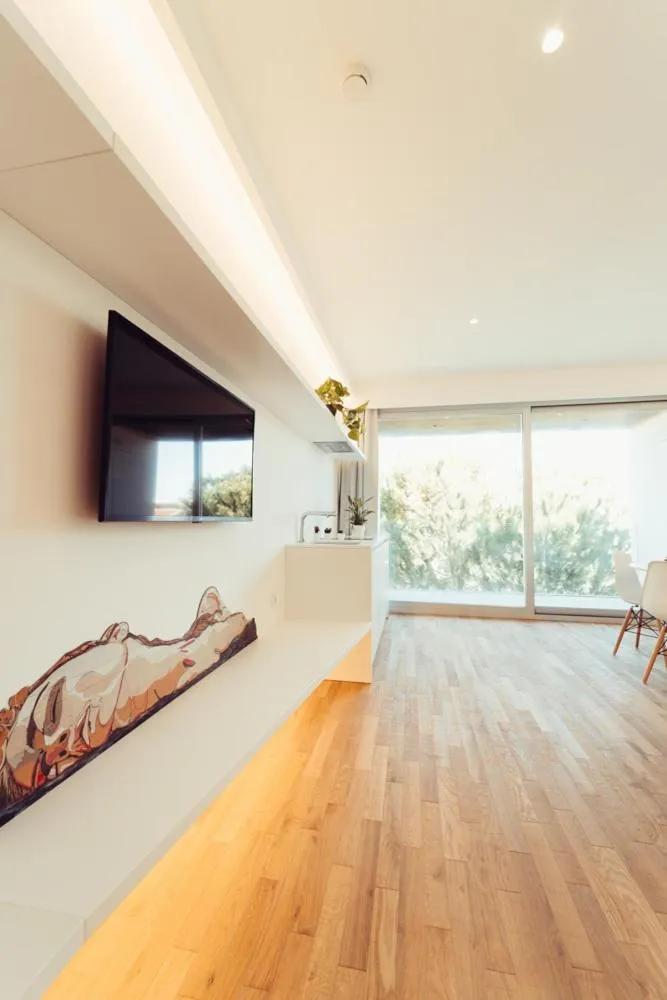 Une télévision murale domine un espace de vie lumineux avec un accès à une terrasse.