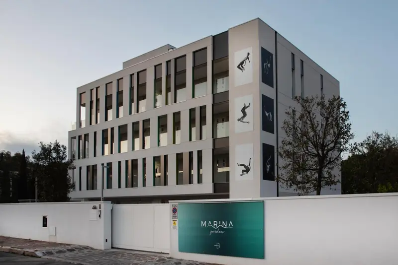 Bâtiment moderne à plusieurs étages avec des ouvertures rectangulaires et des illustrations de nageurs sur la façade.