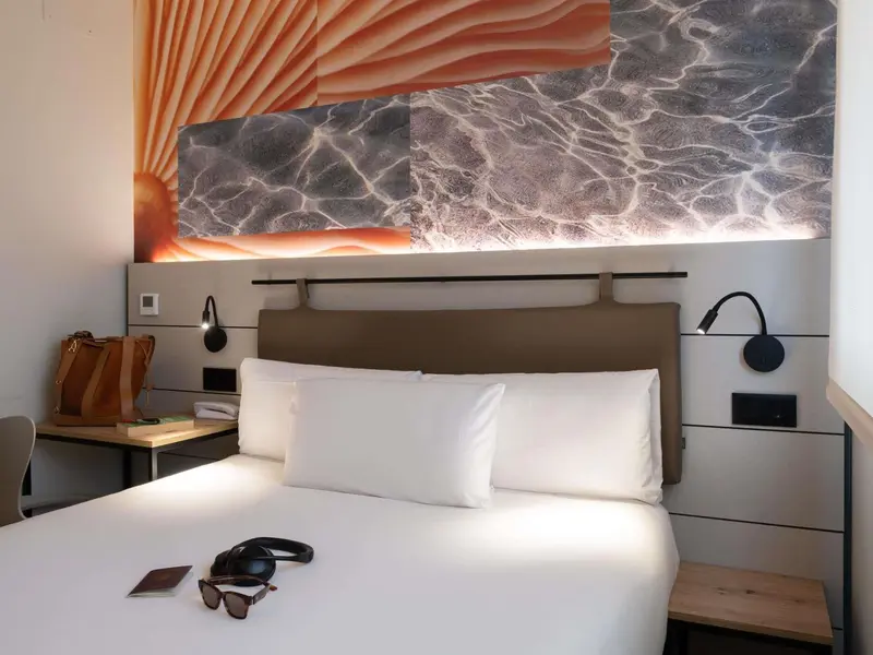 Un lit blanc est dispose dans une chambre avec un decor mural abstrait.