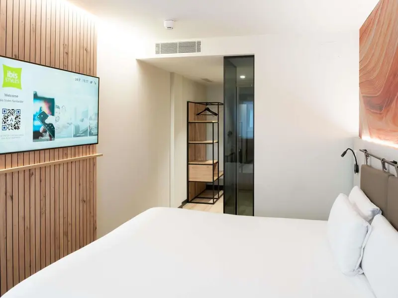 Chambre lumineuse avec un lit blanc et un mur en bois.