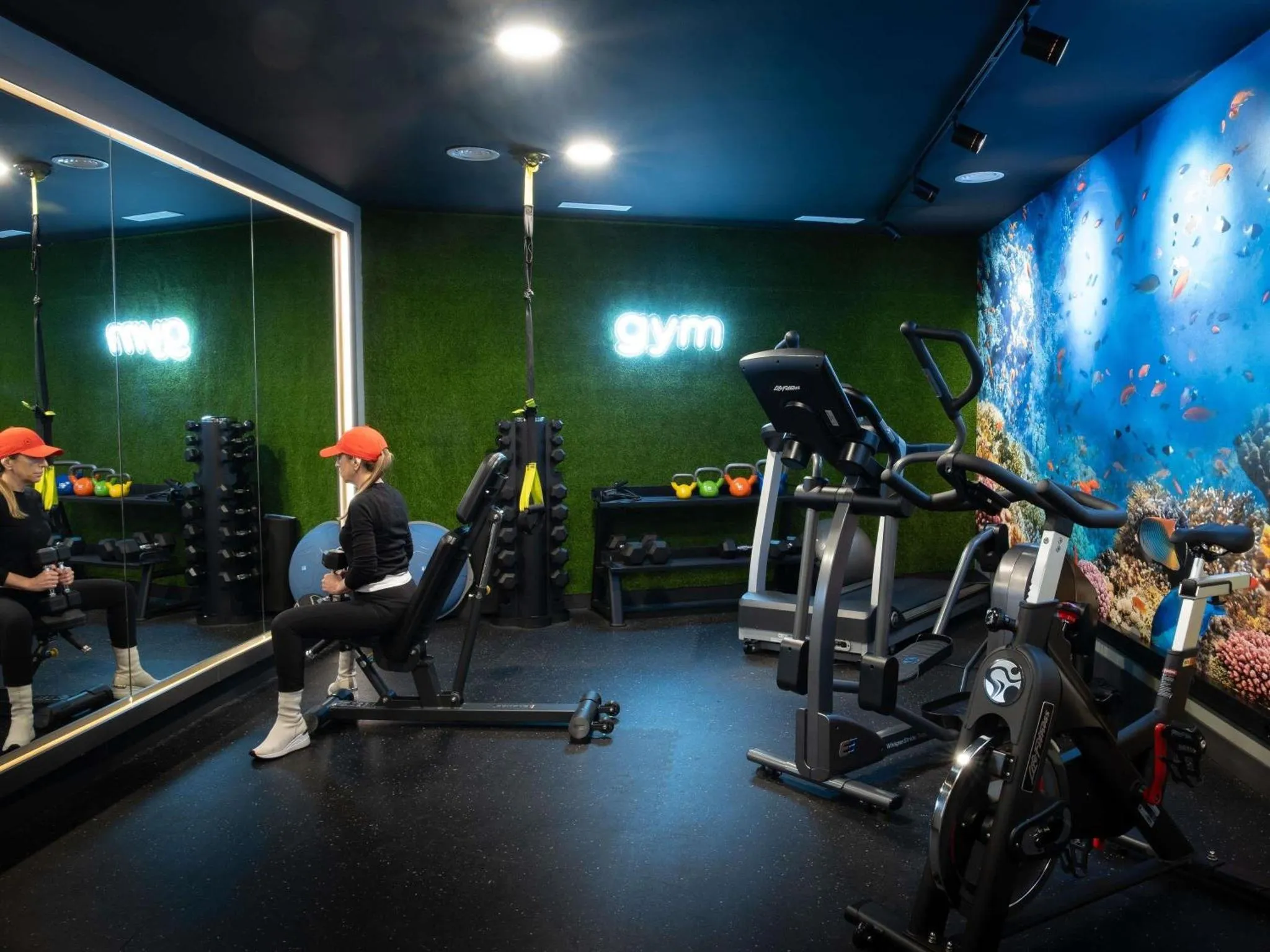 Une salle de sport moderne avec des équipements de musculation et un mur décoré d'un récif corallien.