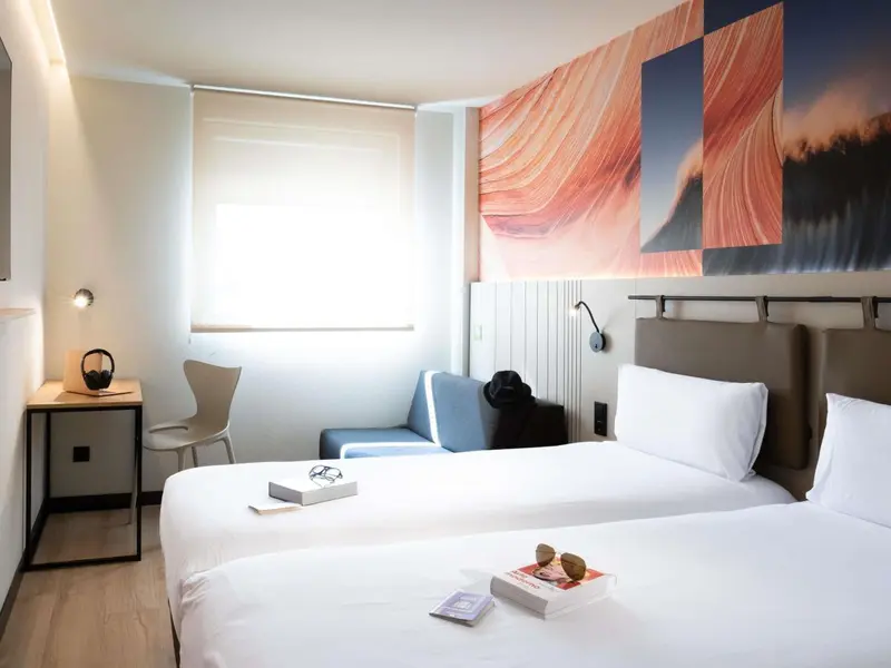 Une chambre lumineuse avec un grand lit et un fauteuil bleu.