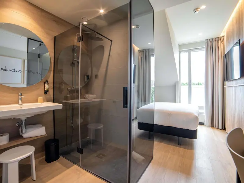 Une salle de bain moderne avec douche à l'italienne et lavabo, donnant sur une chambre lumineuse.