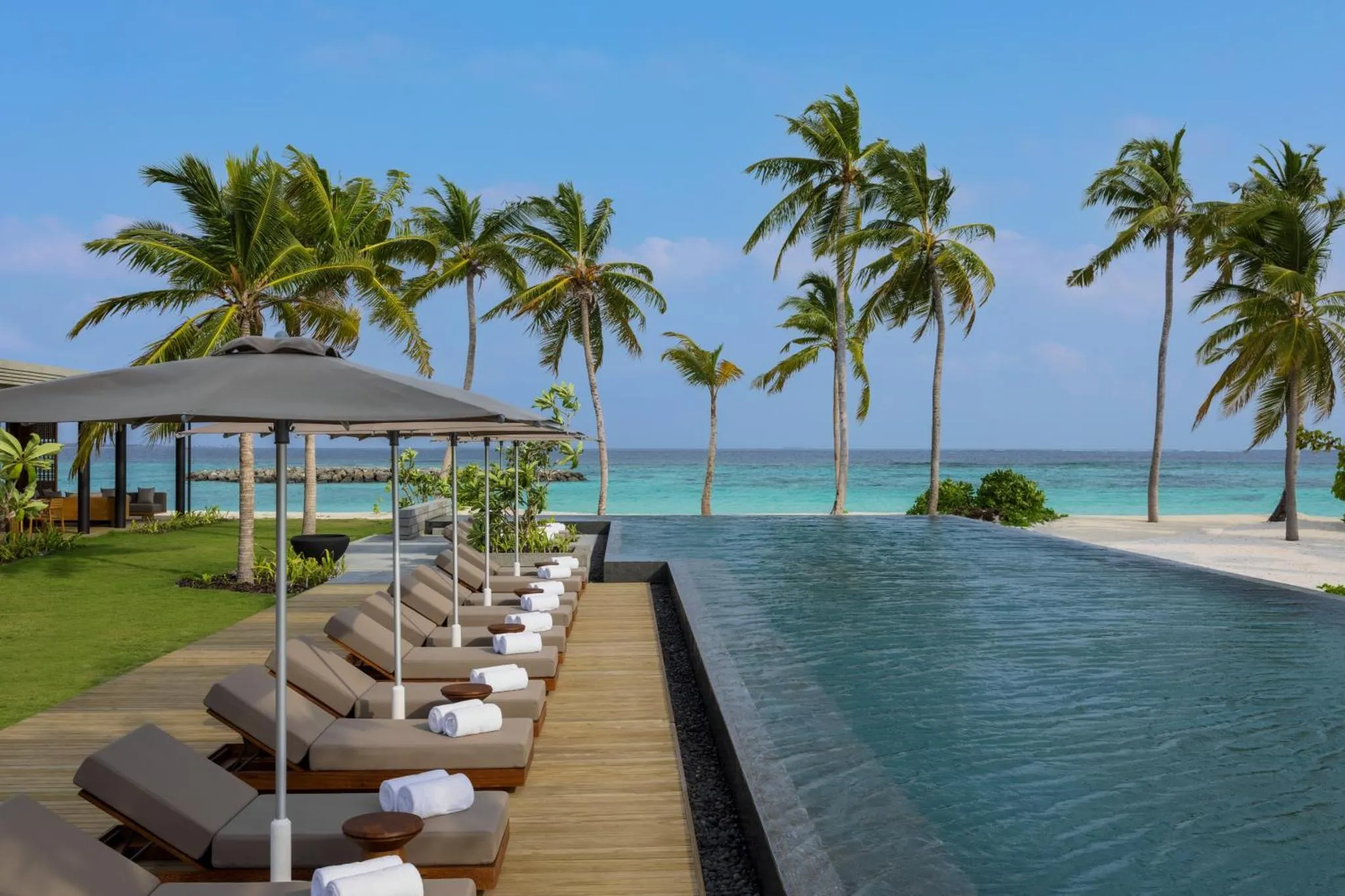 Transats alignés au bord d'une piscine à débordement avec vue sur la mer et la végétation tropicale.