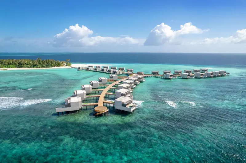 Vue aérienne d'un ensemble de villas sur pilotis au-dessus d'une eau turquoise.