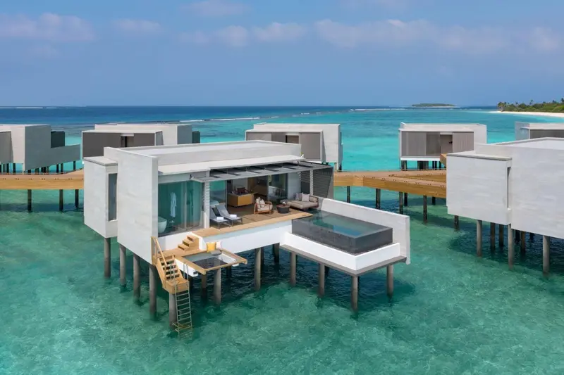Plusieurs bungalows sur pilotis surplombent une eau turquoise et limpide.