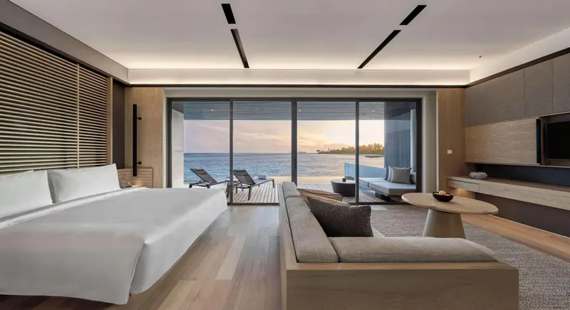 Une chambre lumineuse avec un grand lit et un espace salon donnant sur une terrasse avec vue sur la mer.