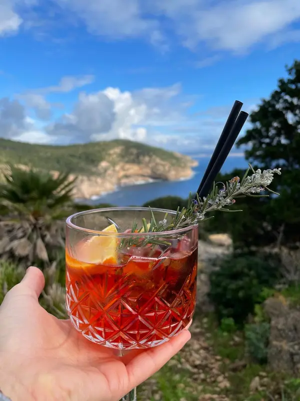Un cocktail coloré est tenu devant un paysage côtier ensoleillé.