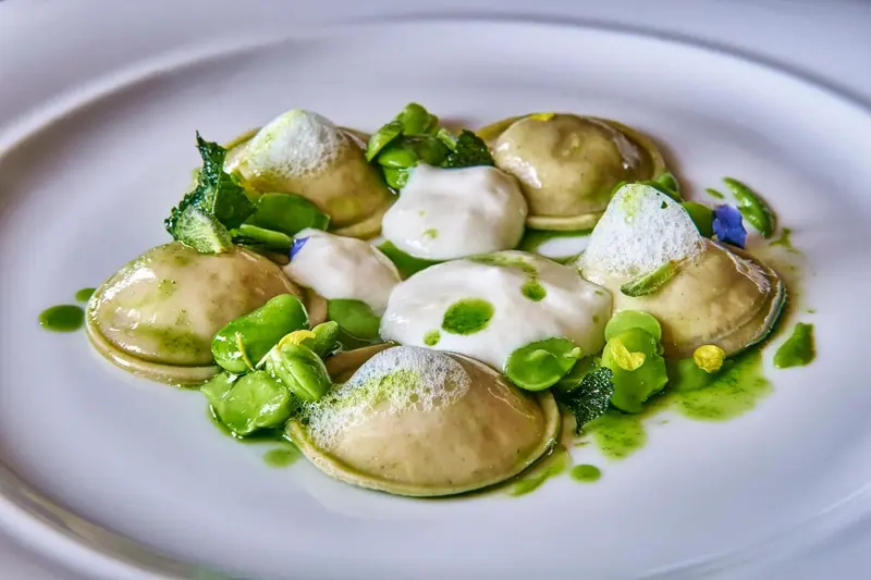 Assiette de raviolis verts et blancs nappés de sauce crémeuse et décorés de jeunes pousses.