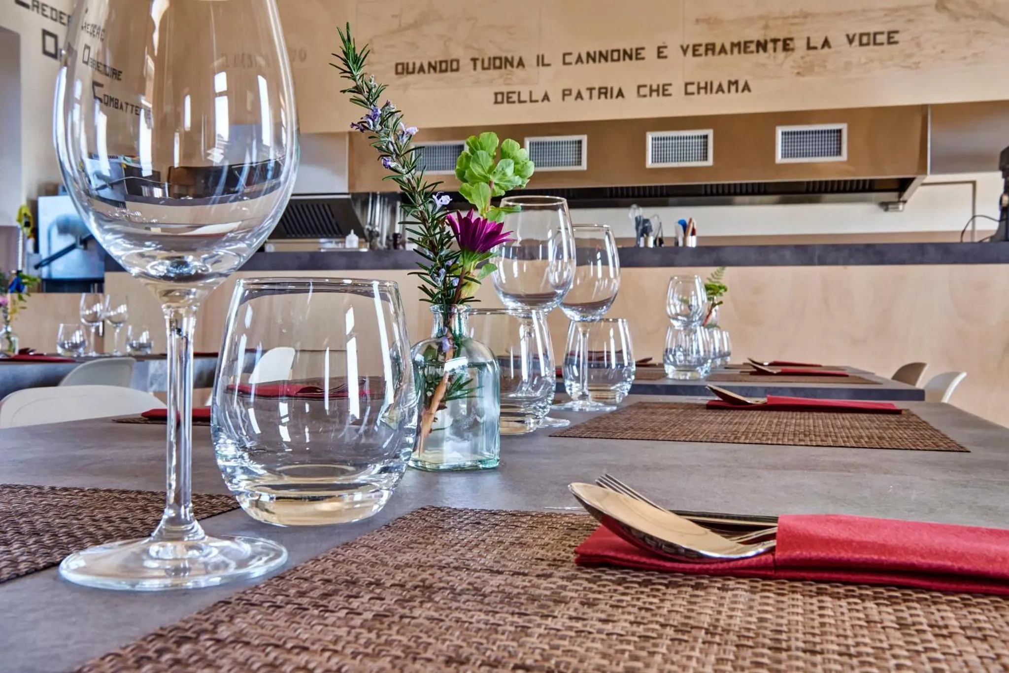 Une table est dressée avec des verres à vin, des couverts et des sets de table.