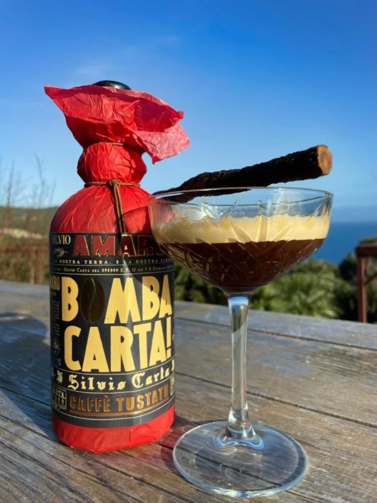 Un verre de boisson est présenté avec une bouteille et une vue sur la mer en arrière-plan.