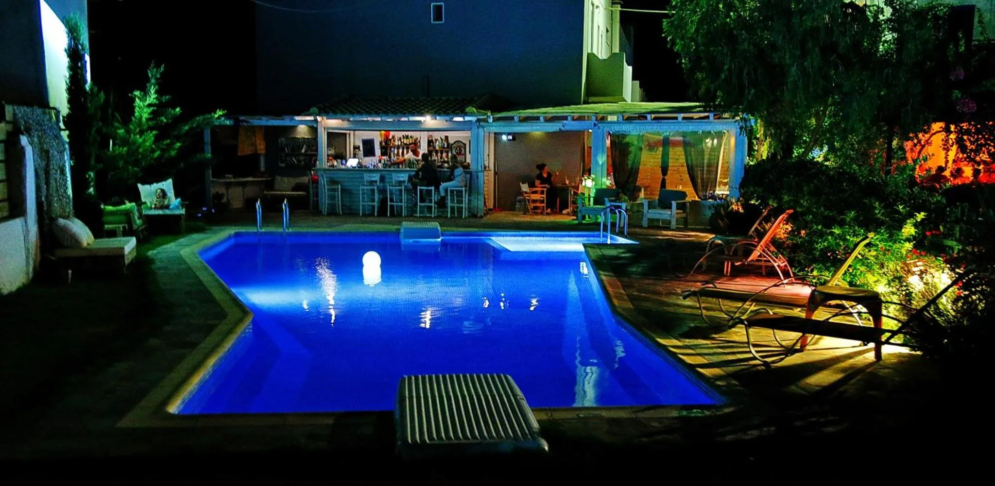 Une piscine illuminée avec un bar en arrière-plan et des transats.
