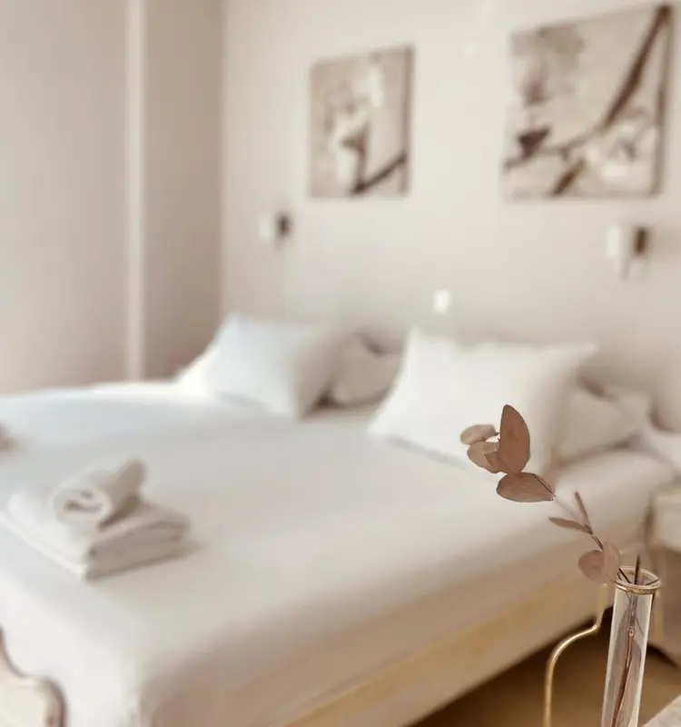 Lit préparé avec linge blanc et décoration florale dans une chambre lumineuse.
