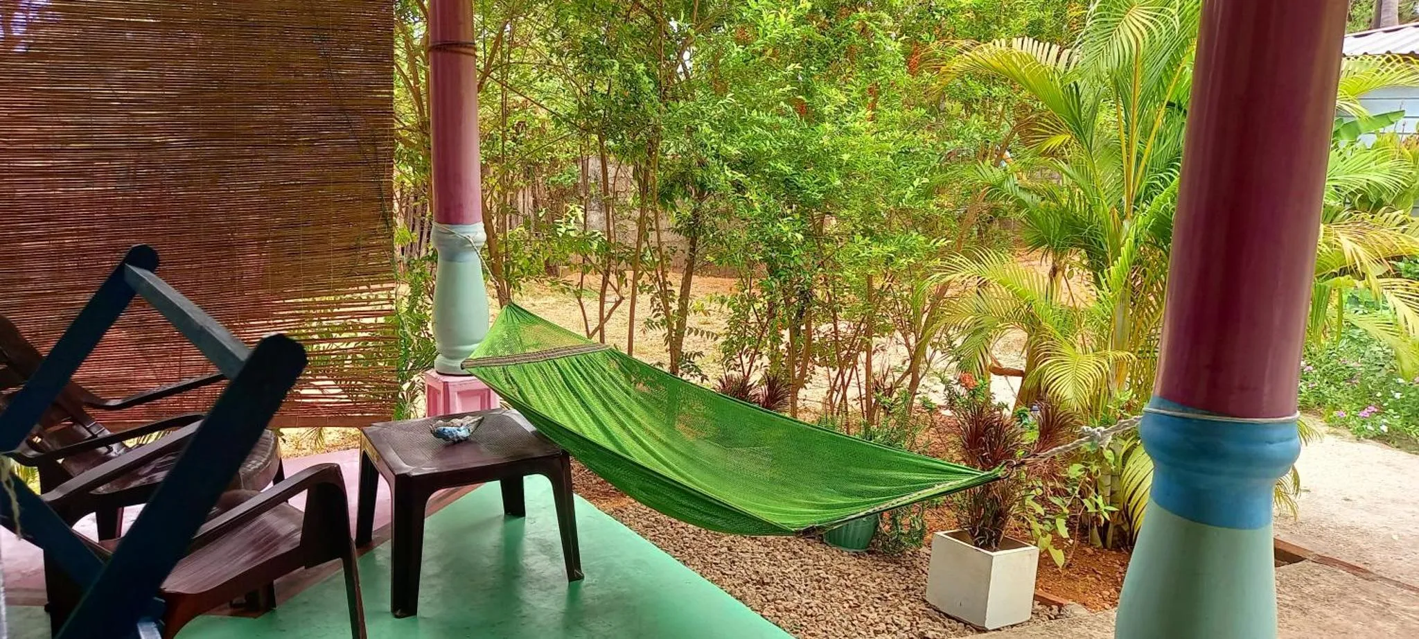 Un hamac vert est suspendu entre deux piliers décorés sur une terrasse.