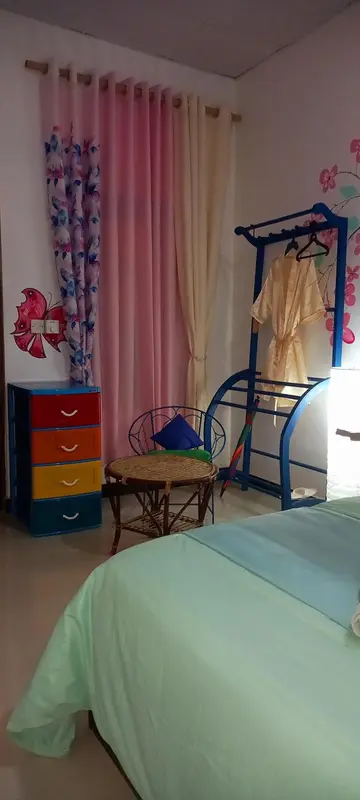 Une chambre lumineuse avec un lit recouvert d'une couverture turquoise et des rideaux roses.