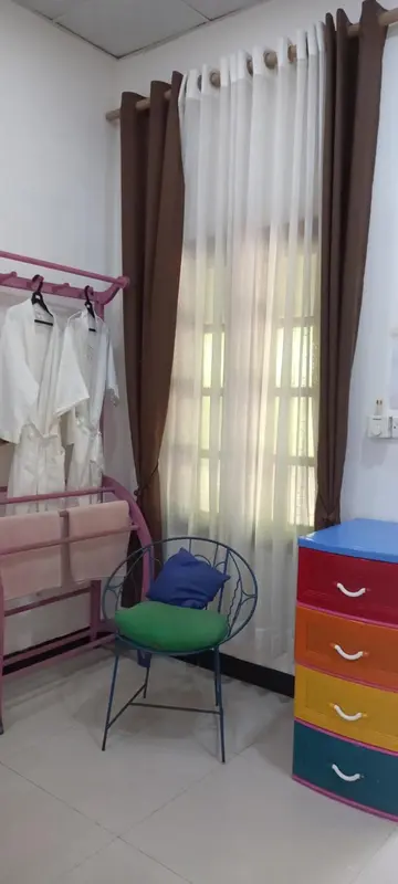 Une chaise et une commode colorée se trouvent près d'une fenêtre avec des rideaux.