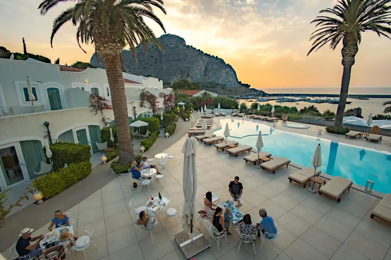 Vue aérienne d'une piscine avec des transats et des tables à manger près d'un bâtiment blanc.