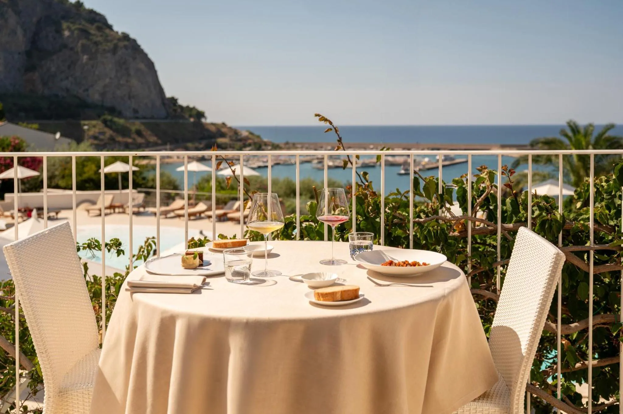 Table dressée avec des verres de vin et des assiettes en terrasse avec vue sur la mer.