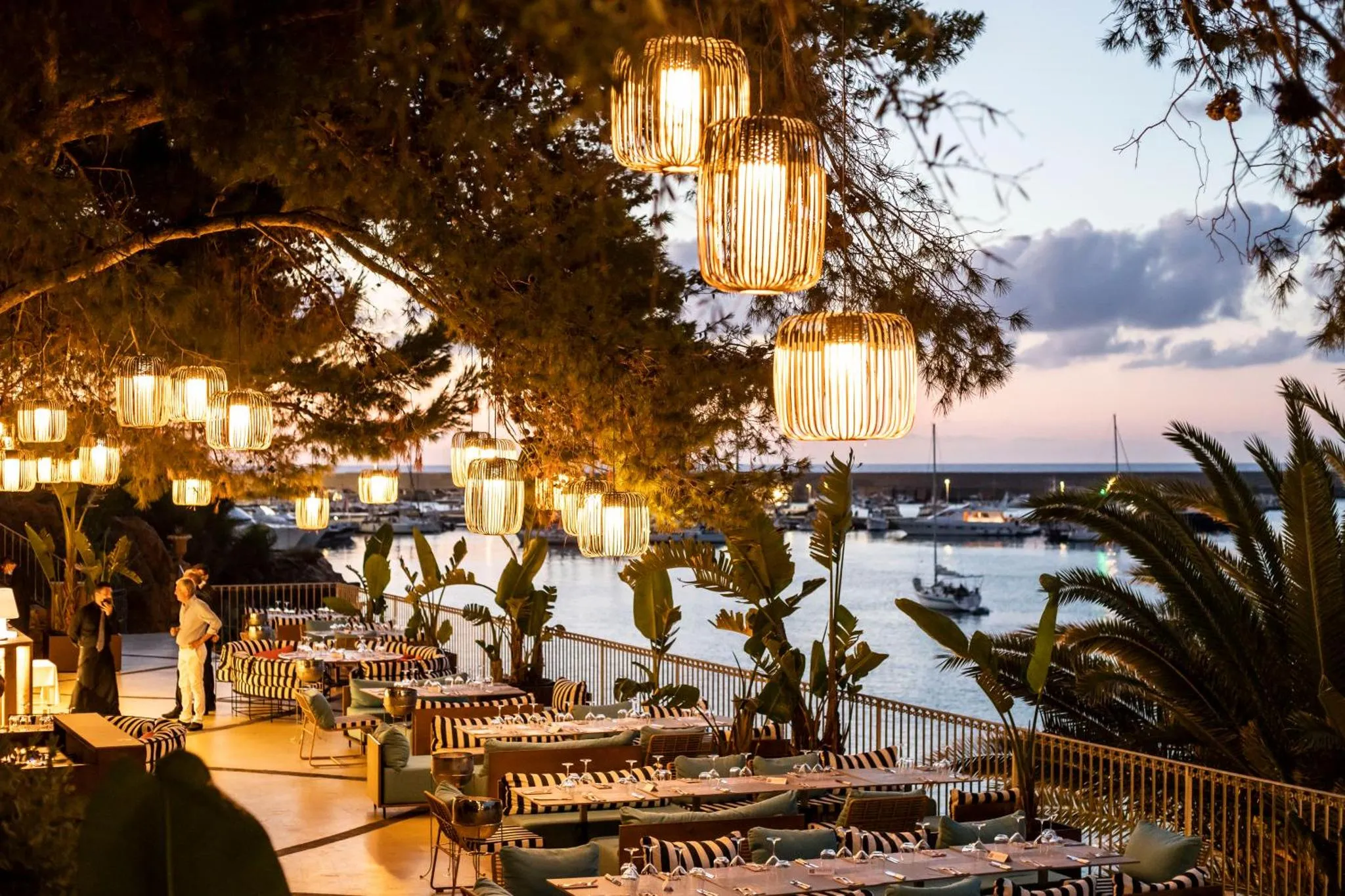 Terrasse illuminée avec tables dressées face à la mer au coucher du soleil.