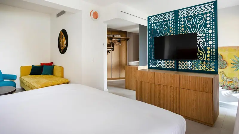 Une chambre lumineuse avec un canapé jaune et un grand lit blanc.