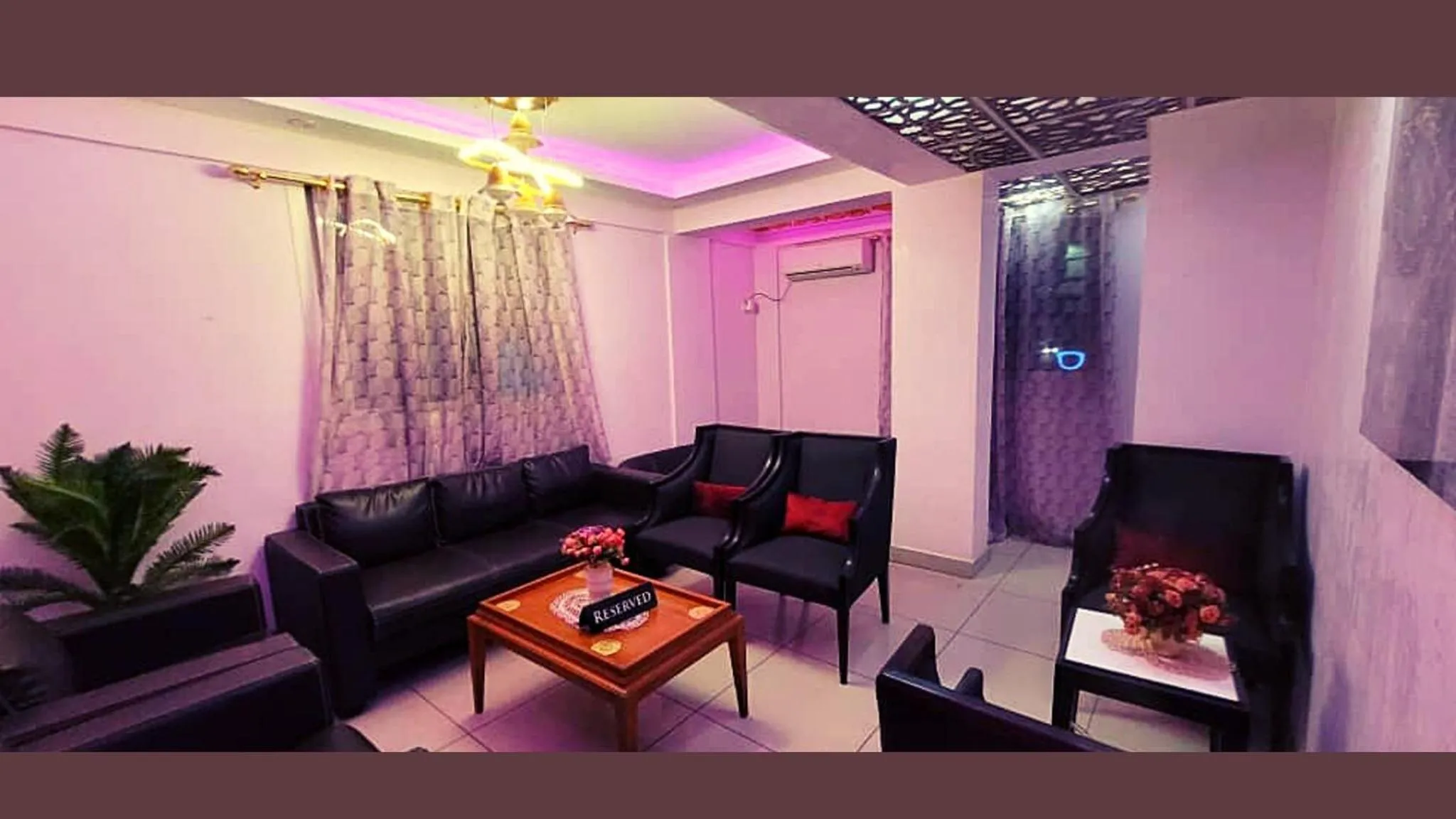 Un salon avec canapés et fauteuils noirs, éclairé de lumières roses et violettes.