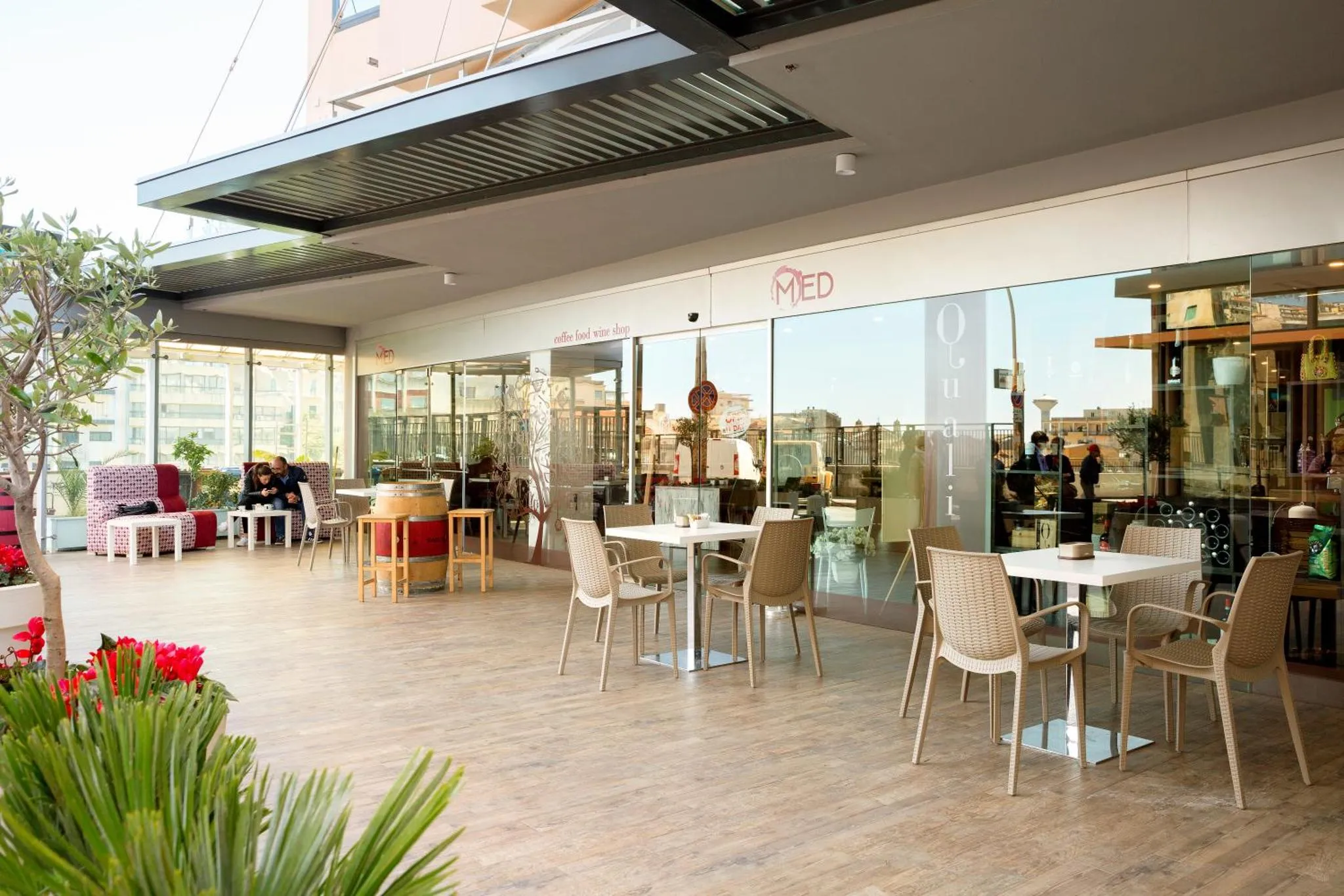 Terrasse ombragée avec tables et chaises, donnant sur une vue urbaine.