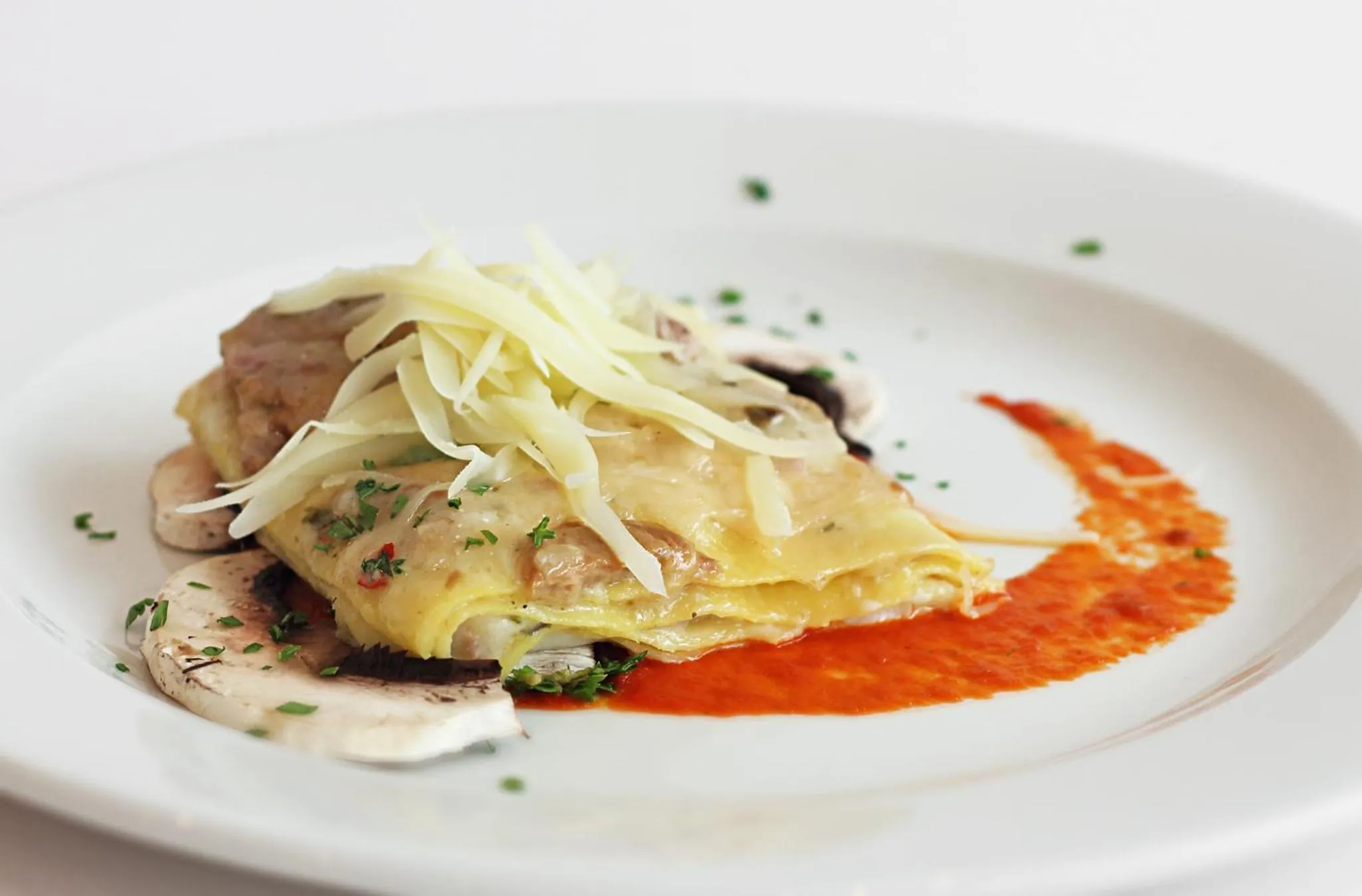 Assiette de lasagnes à la crème et à la sauce tomate, décorée de persil frais.