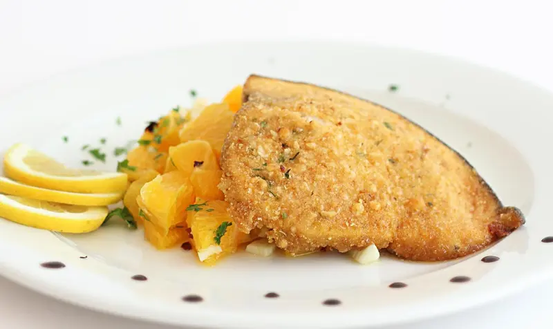 Un plat de poisson pané servi avec des agrumes et un filet de citron.
