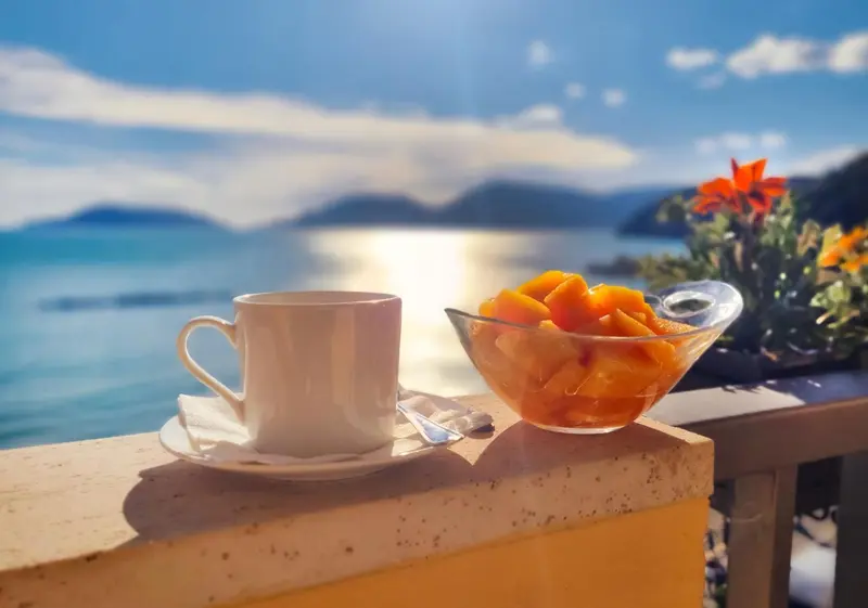 Une tasse de café et un saladier de fruits frais sur une table au bord de l'eau.