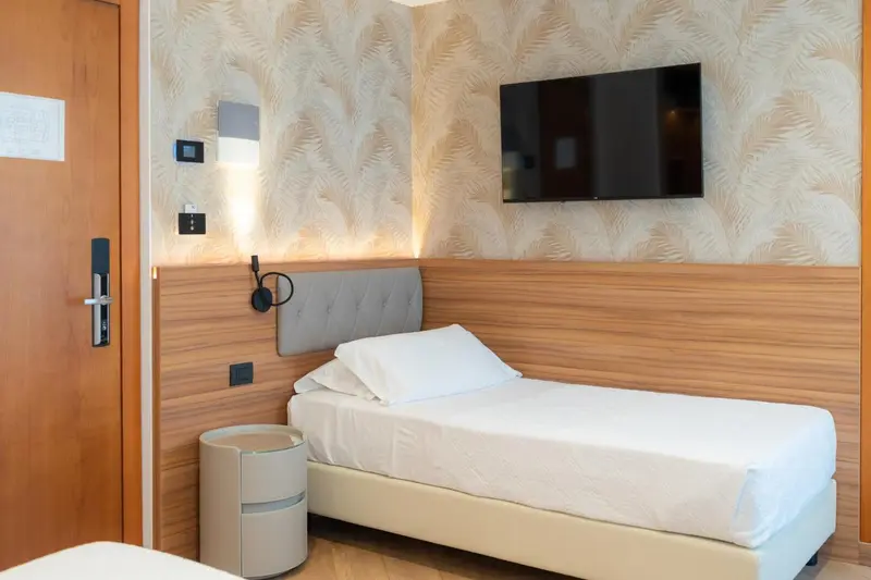 Une chambre lumineuse avec un lit simple et un téléviseur mural.