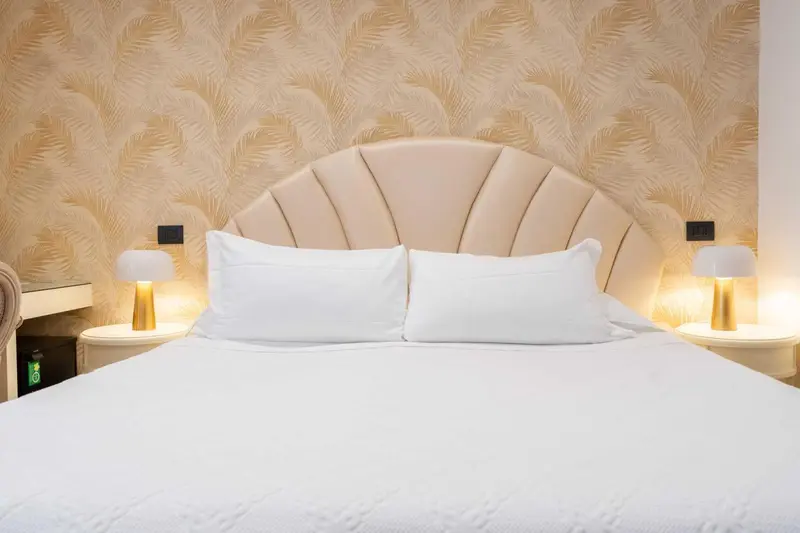 Un lit double avec une tête de lit beige et des oreillers blancs est présenté dans une chambre.