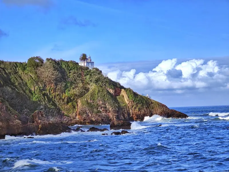 Côte rocheuse avec végétation et un bâtiment au sommet d'une falaise.