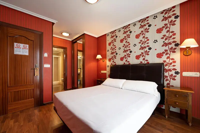 Une chambre d'hôtel avec un grand lit et un décor mural rouge et floral.