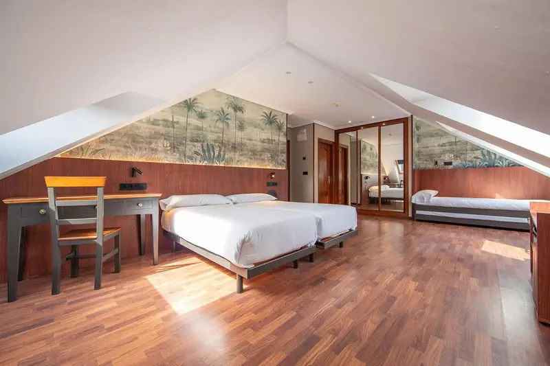 Une chambre mansardée lumineuse avec deux lits simples et un bureau.