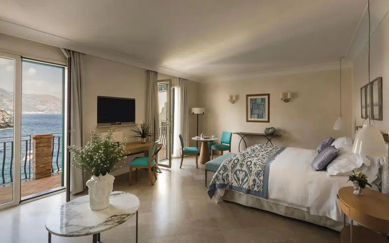 Une chambre lumineuse avec un lit et un coin salon donnant sur la mer.