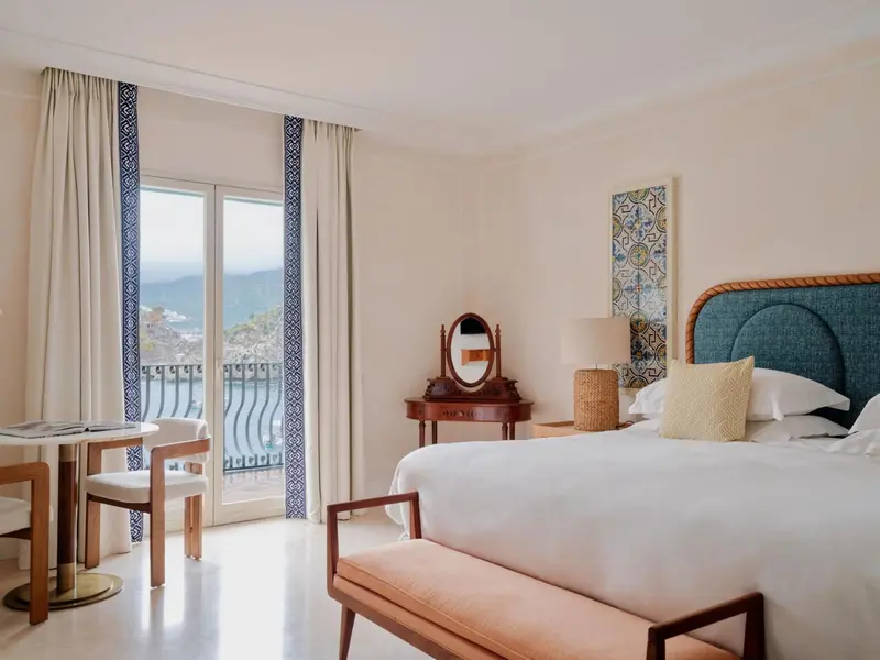 Chambre lumineuse avec un lit blanc et une vue sur la mer.