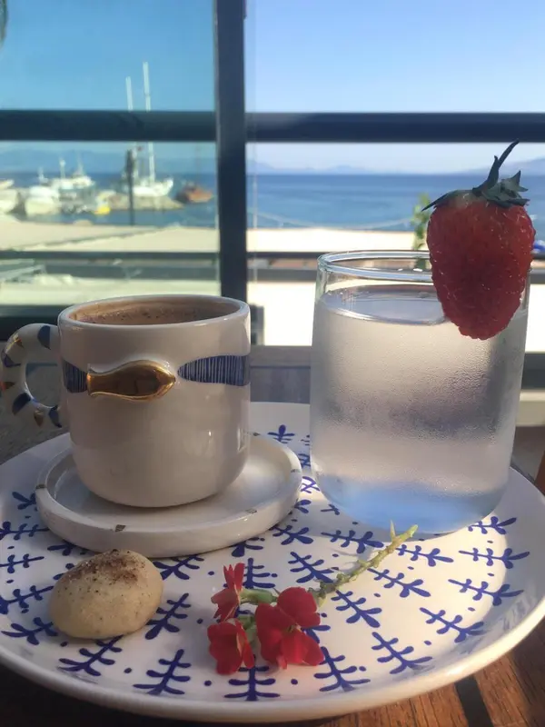 Une table est dressée avec une boisson et des fruits frais, offrant une vue sur la mer et un port.