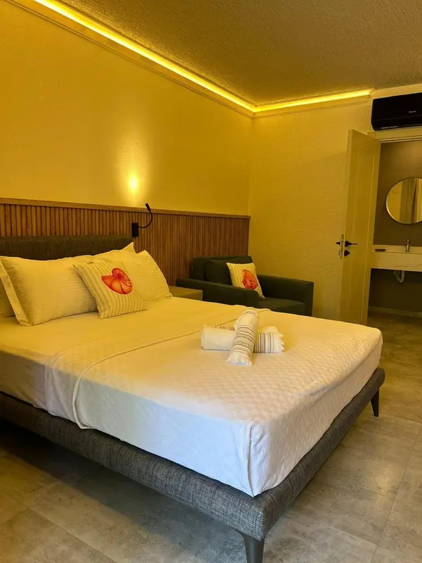 Une chambre lumineuse avec un grand lit recouvert d'une courtepointe blanche et de coussins décorés.