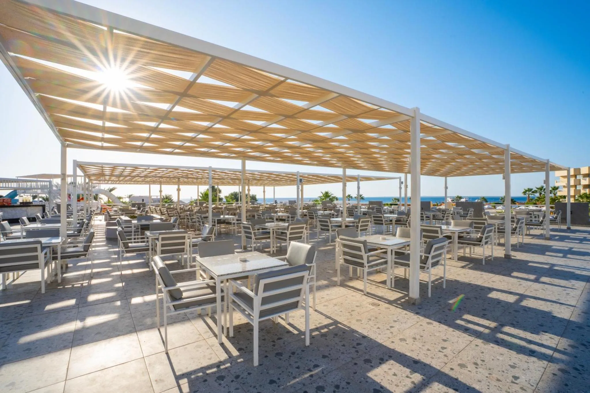 Terrasse ombragée avec tables et chaises en métal face à la mer.