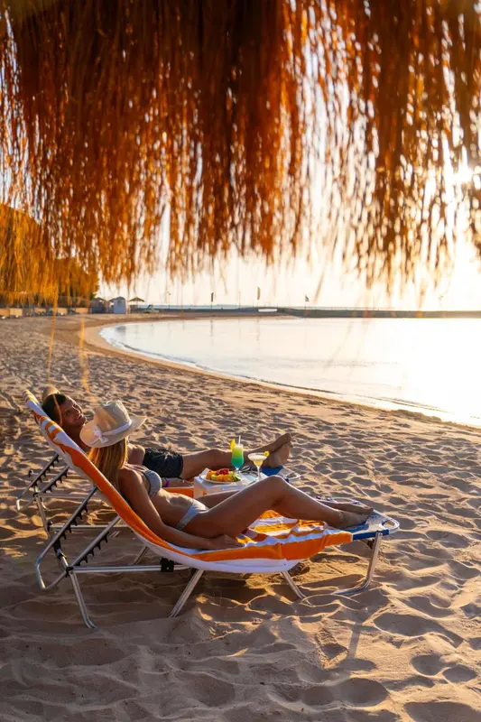 Une femme se relaxe sur une chaise longue sur une plage de sable fin au coucher du soleil.