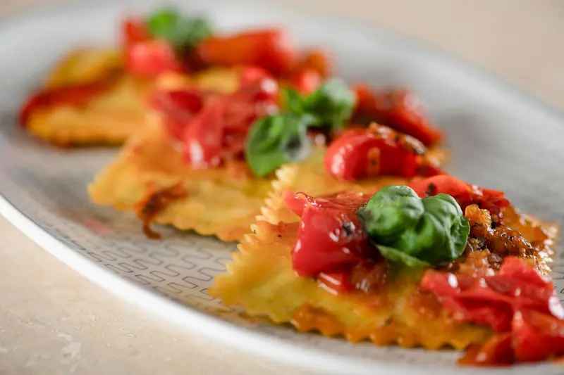 Assiette de raviolis garnis de tomates cerises et de basilic frais.
