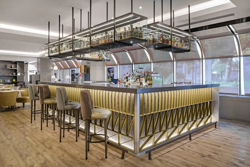 Un long comptoir de bar moderne avec des tabourets est éclairé par des luminaires suspendus.