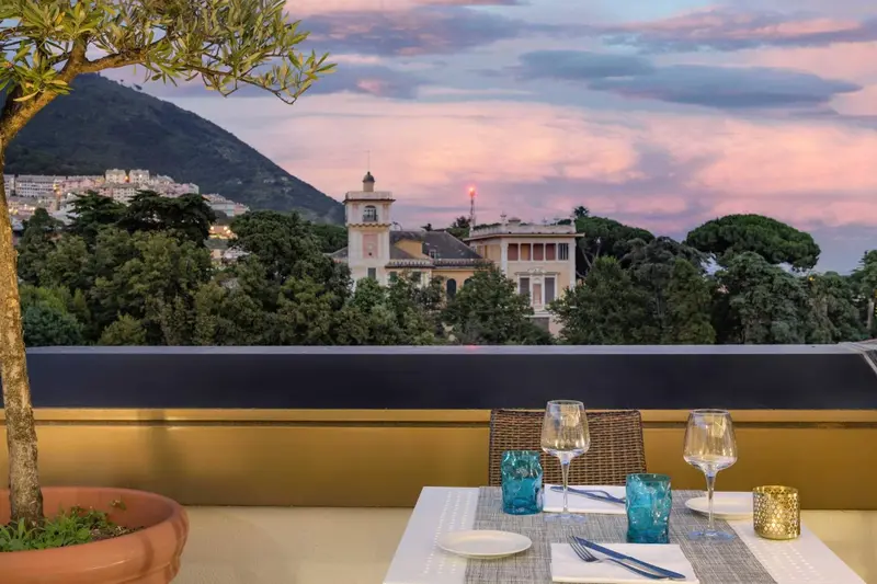 Table dressée sur une terrasse avec vue sur une ville côtière au coucher du soleil.