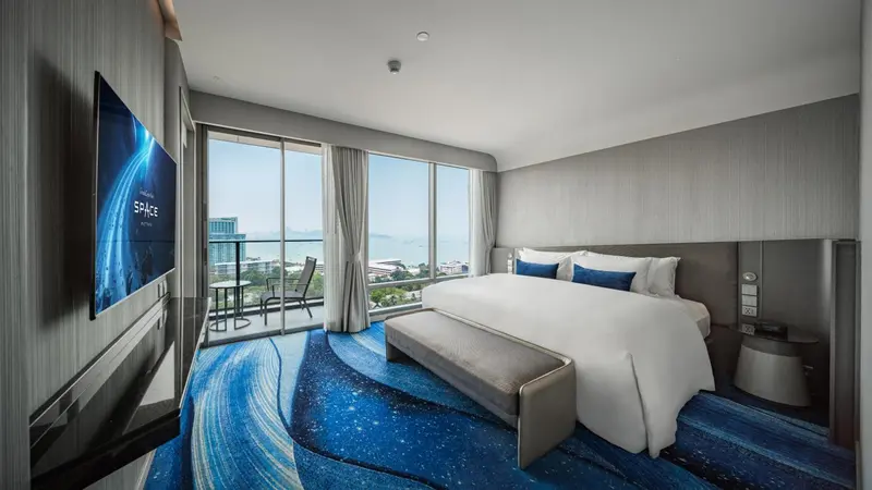 Chambre spacieuse avec un grand lit et une vue sur la mer depuis un balcon.