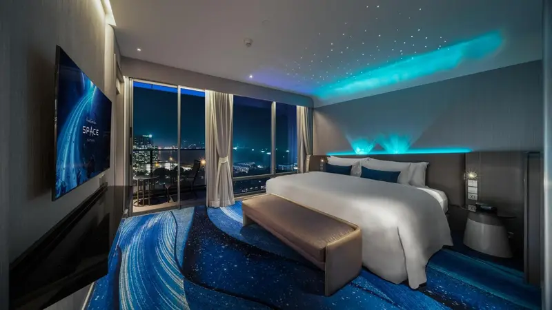 Chambre moderne avec un grand lit et une vue nocturne sur la ville.