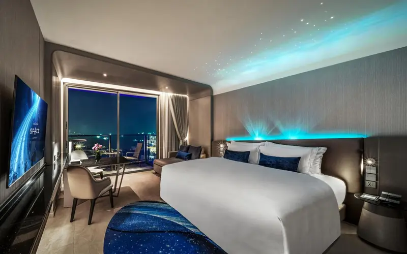 Chambre moderne avec un grand lit et une vue nocturne sur la ville.