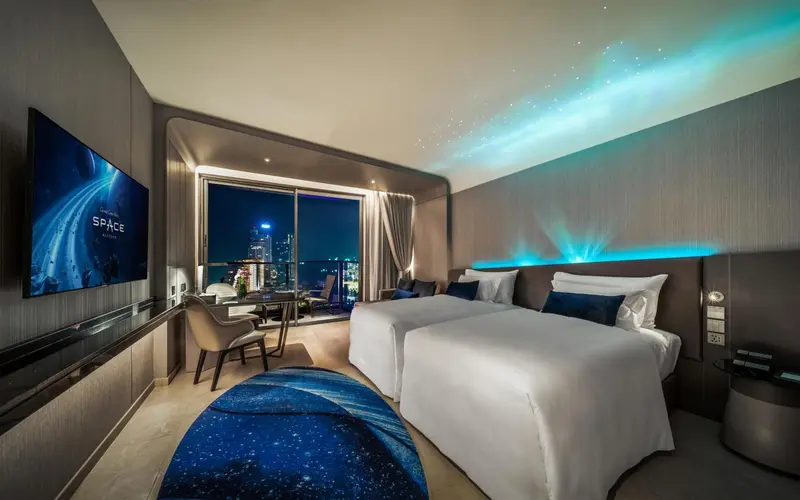 Chambre moderne avec deux lits simples et vue sur la ville la nuit.