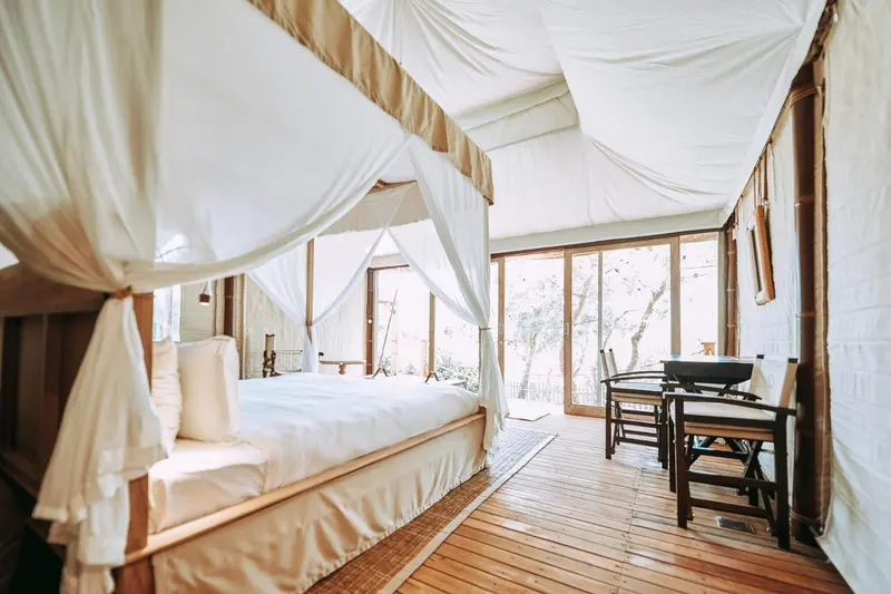 Une chambre lumineuse avec un grand lit à baldaquin et une terrasse en bois.