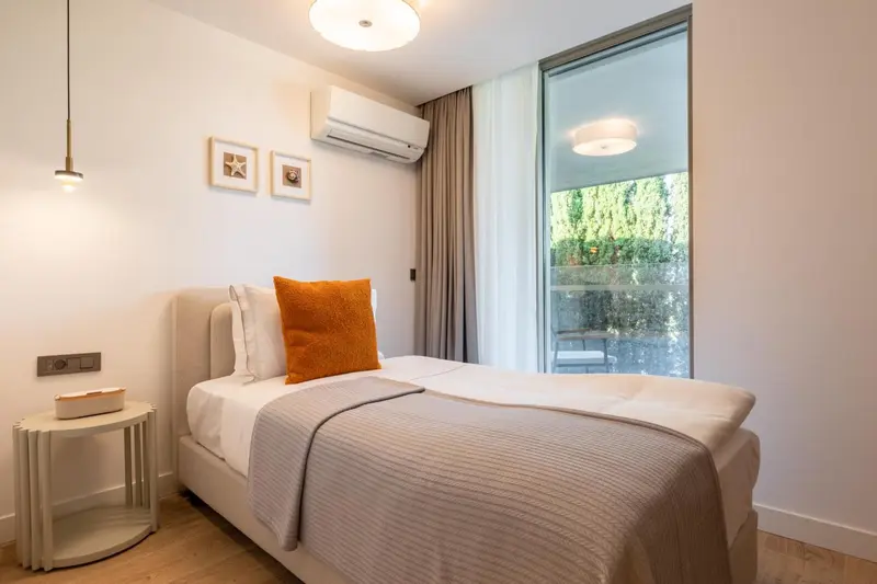 Une chambre lumineuse avec un lit simple et un oreiller orange.